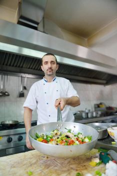 Handsome chef dressed in white uniform decorating pasta salad and seafood fish in modern kitchen