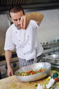 Handsome chef dressed in white uniform decorating pasta salad and seafood fish in modern kitchen