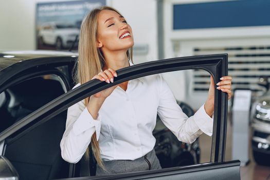 Beautiful young woman touching her new car with pleasure and joy