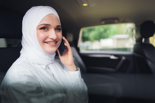 Beautiful young woman in hijab sitting in a car and talking on the phone, close up