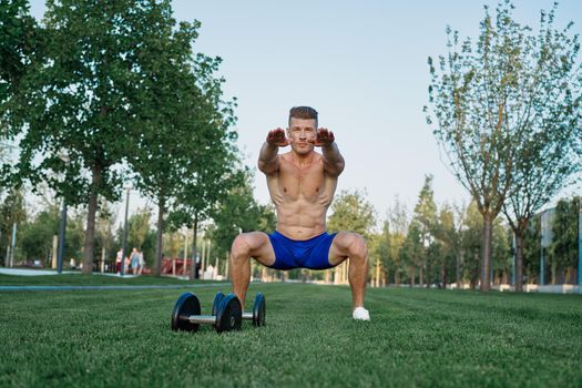 Muscled man in the park training with dumbbells. High quality photo