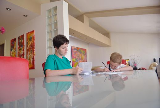 young mom woman doing home work with elementary school grade boy at home in kitchen