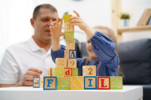 Grandfather and granddaughter playing wooden cubes in living room at home