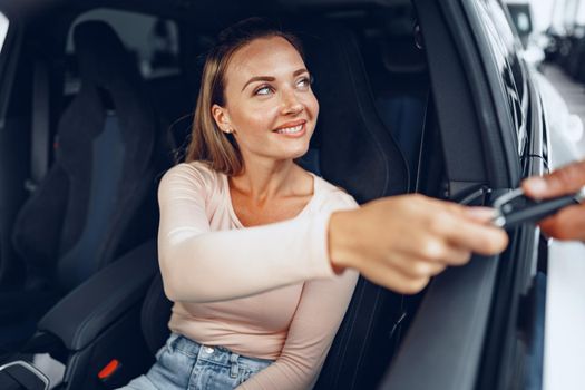 Young attractive caucasian woman sits in her newly bought car in dealership