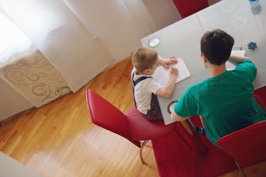 young mom woman doing home work with elementary school grade boy at home in kitchen