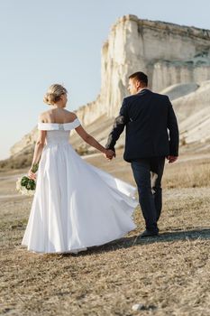 Bride and groom standing against big white rock in a field