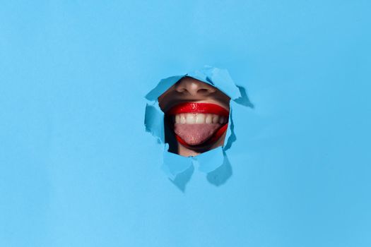 woman peeping through the holes in the poster blue studio background. High quality photo