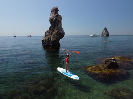 Young attractive brunette woman in red swimsuit, swimming on kayak around volcanic rocks, like in Iceland. Back view. Christmas holiday vacation and travel concept.