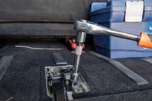 A man's hand unscrews the nut in the car interior with a ratchet. Specialist Unscrews Bolts Close-up.