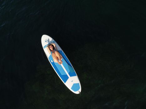 Young attractive brunette woman in red swimsuit, swimming on kayak around volcanic rocks, like in Iceland. Back view. Christmas holiday vacation and travel concept.