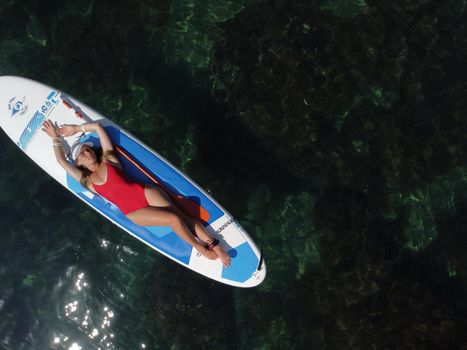 Young attractive brunette woman in red swimsuit, swimming on kayak around volcanic rocks, like in Iceland. Back view. Christmas holiday vacation and travel concept.