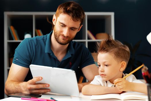 Young boy sitting with his father at the table and using laptop for study