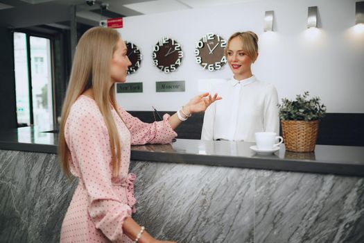 Blonde woman hotel guest checking-in at front desk in hotel close up