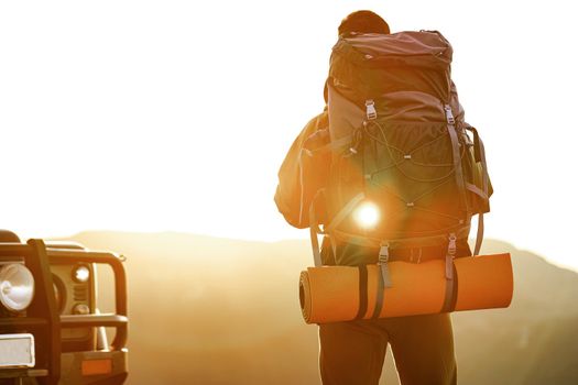 Portrait of a young traveler man in hiking equipment standing near his off-road car at dawn