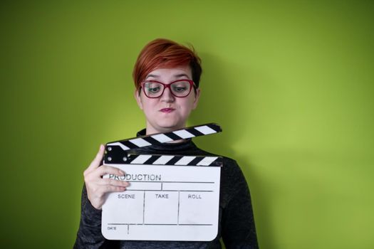 redhead woman holding movie clapper isolated against green background cinema concept in studio