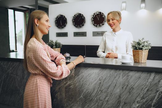 Blonde woman hotel guest checking-in at front desk in hotel close up
