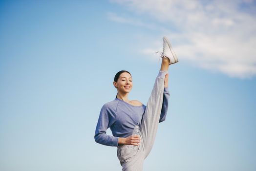 Beautiful girl training on a sky background. Woman in a blue sweater. Lady make a yoga. Girl with a bootle of water