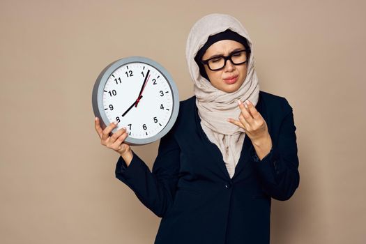 woman in hijab with clock in hands work office beige background. High quality photo