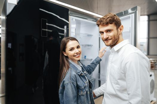 Young couple selecting new refrigerator in household appliance store, close up