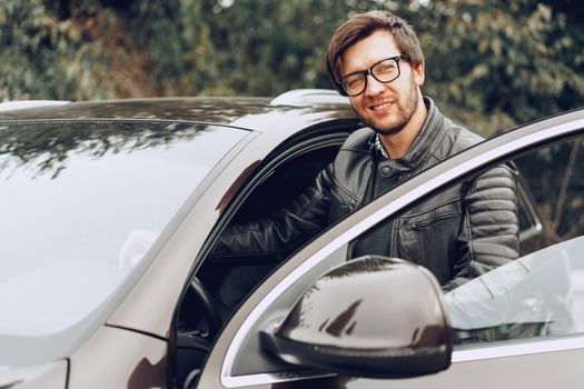 Stylish man in glasses sits in a car, close up portrait