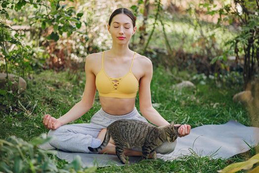 Beautiful girl training on a yard. Woman in a yellow top. Lady make a yoga. Girl with cute cat.