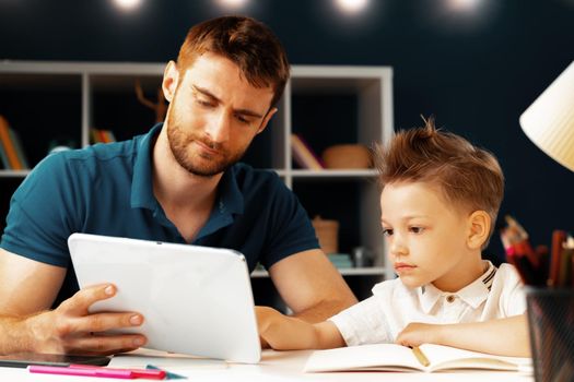 Young boy sitting with his father at the table and using laptop for study