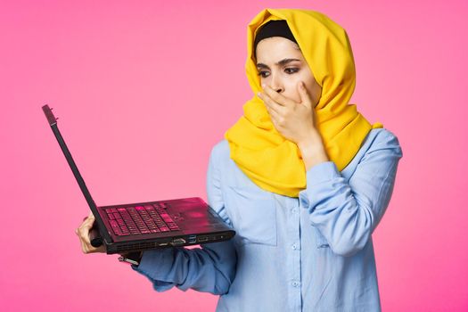 muslim woman in yellow hijab with laptop technology student pink background. High quality photo