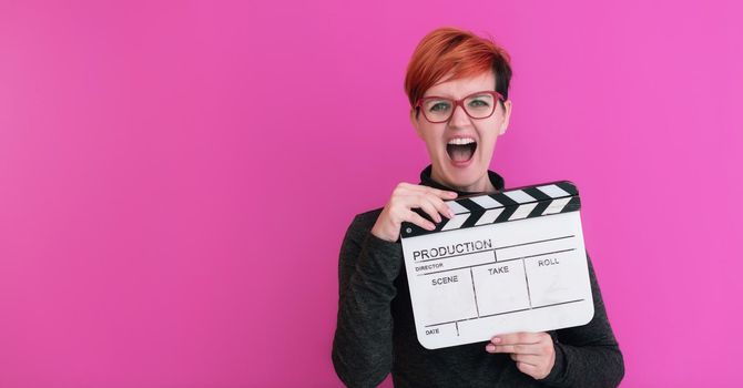 redhead woman holding movie clapper isolated against pink background  cinema concept in studio