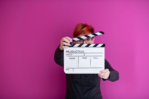 redhead woman holding movie clapper isolated against pink background cinema concept in studio