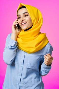 muslim woman in yellow hijab talking on the phone pink technology background. High quality photo