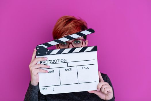 redhead woman holding movie clapper isolated against pink background cinema concept in studio