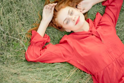 cheerful woman in a red dress lies on the grass top view. High quality photo