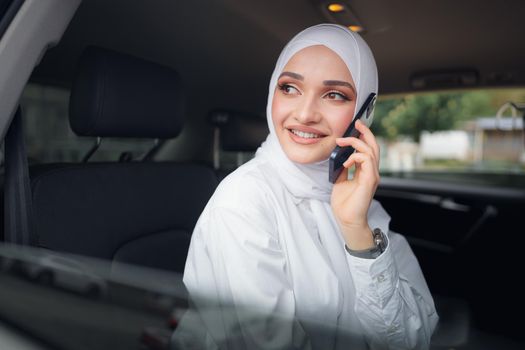 Beautiful young woman in hijab sitting in a car and talking on the phone, close up