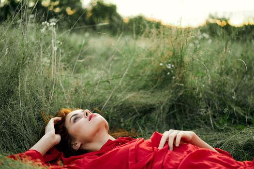 pretty woman in red dress lies on the grass freedom landscape. High quality photo