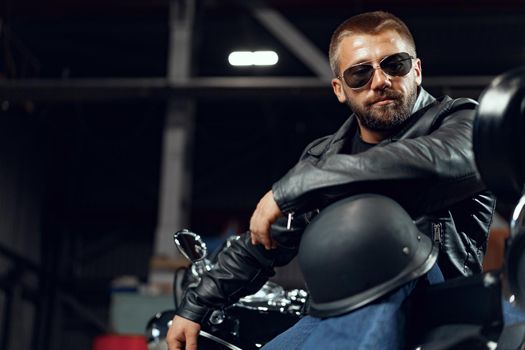Portrait of bearded man motocyclist in dark sunglasses on dark building background
