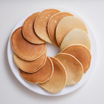 Plate with many round pancakes standing on white background top view. Delicious breakfasts concept