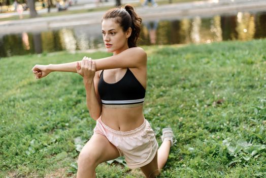 Young woman stretches her arms while doing sports in the park.