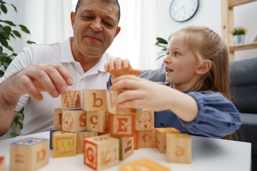 Grandfather and granddaughter playing wooden cubes in living room at home