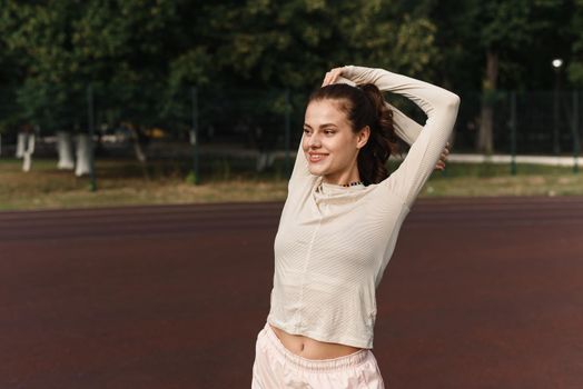 Young woman stretches her arms while playing sports in the stadium.