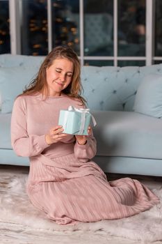 Beautiful middle-aged woman excited opening Christmas presents near the Christmas tree on Christmas eve