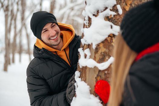 Young loving couple play hide and seek in a snowy winter park close up