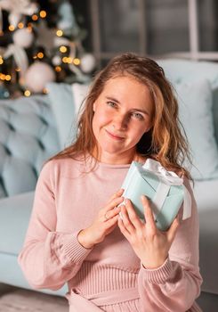 Beautiful middle-aged woman excited opening Christmas presents near the Christmas tree on Christmas eve