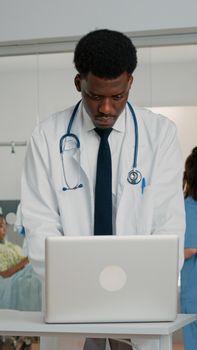 Doctor using laptop to treat patient in hospital ward while nurse helping with checkup files. Medic working with modern device to find healthcare information about treatment and medicine