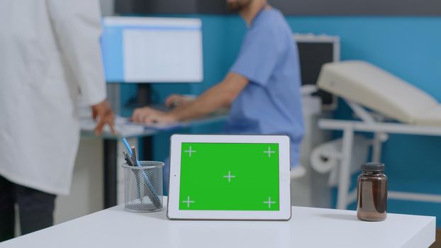 Closeup of mock up green screen chroma key tablet computer with isolated display standing on desk in hospital office. Multiethnic medical team analyzing sickness report working at healthcare treatment