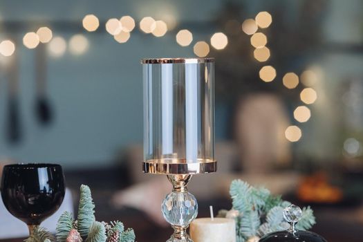 Close up of high glass candlestick on table near Christmas decoration. New Year eve concept