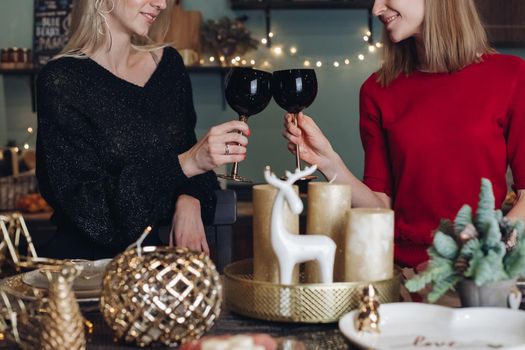 Pretty smiling ladies toasting with wine glasses while celebrating Christmas at home