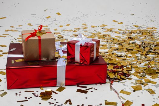 Floor covered with gold confetti. Big gift box on the floor with two smaller presents on the top of it. New year and happy holiday concept