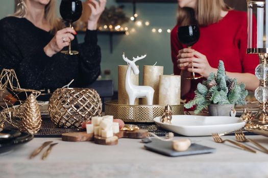 Pretty smiling ladies toasting with wine glasses while celebrating Christmas at home