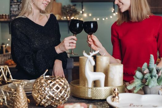 Pretty smiling ladies toasting with wine glasses while celebrating Christmas at home