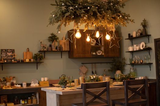 View over dining table served for winter Christmas dinner under decorative illuminations with festive stars and fir tree branches. Christmas dinner concept.